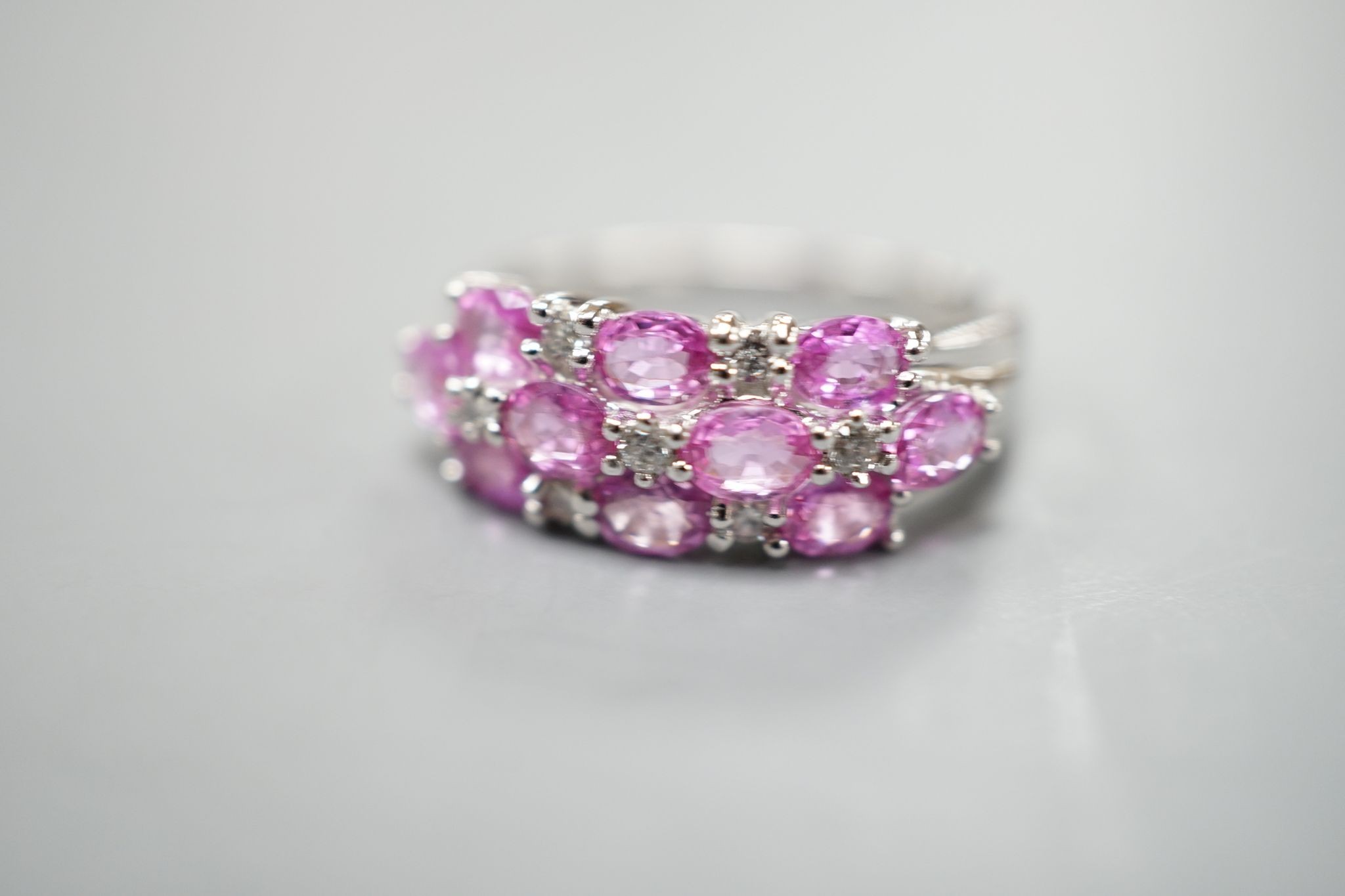 A modern 14k white metal, pink sapphire and diamond cluster set half hoop dress ring, size O, gross weight 4.6 grams.